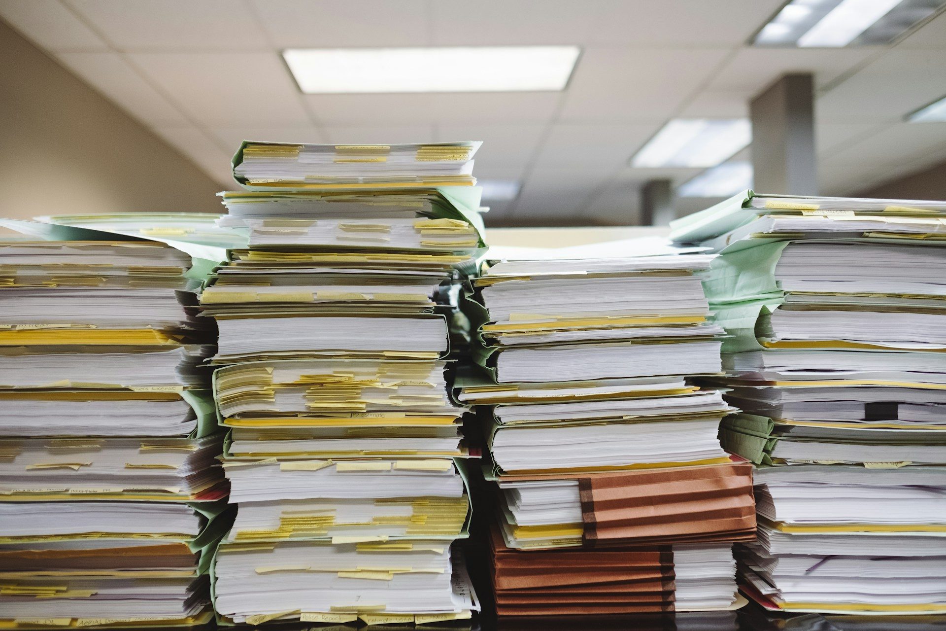 Piles de dossiers papier annotés de marque-pages jaunes dans un bureau